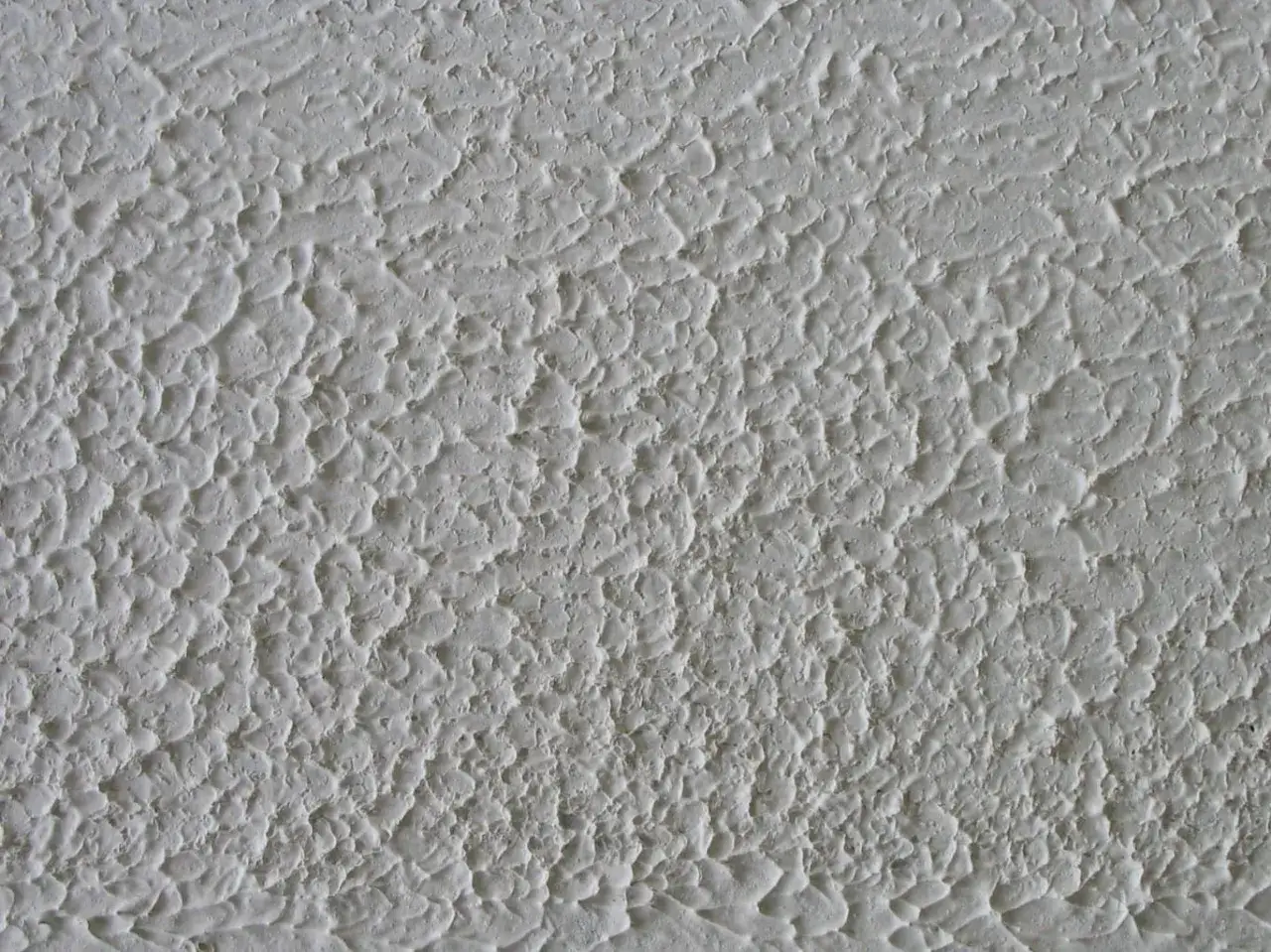 Texture de crépi blanc, rugueuse et irrégulière. Idéal pour comprendre comment enlever du crépi et rénover un mur.