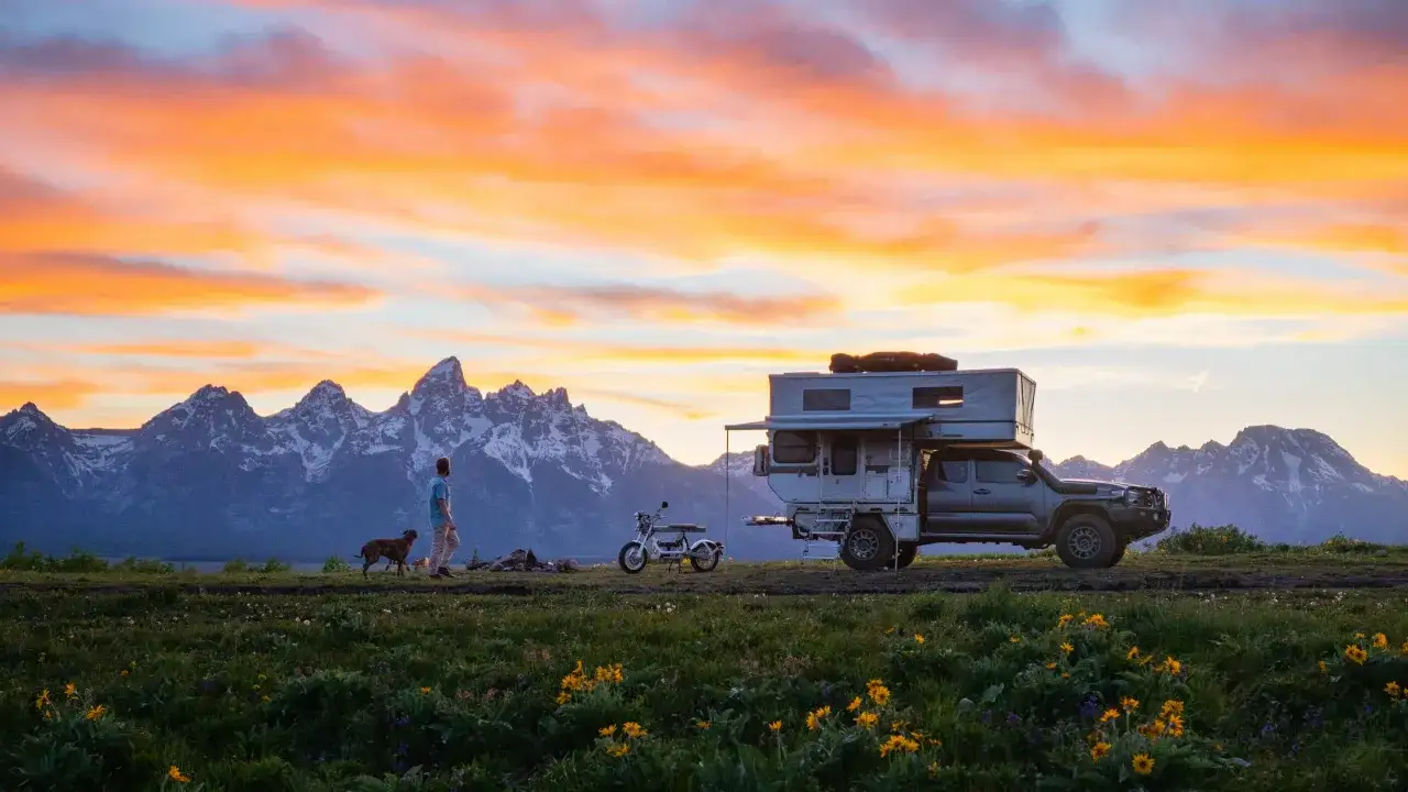 Mann mit Hund und Wohnmobil vor Bergkulisse bei Sonnenuntergang. Perfekte mai reiseziele f&uuml;r Abenteuerlustige.
