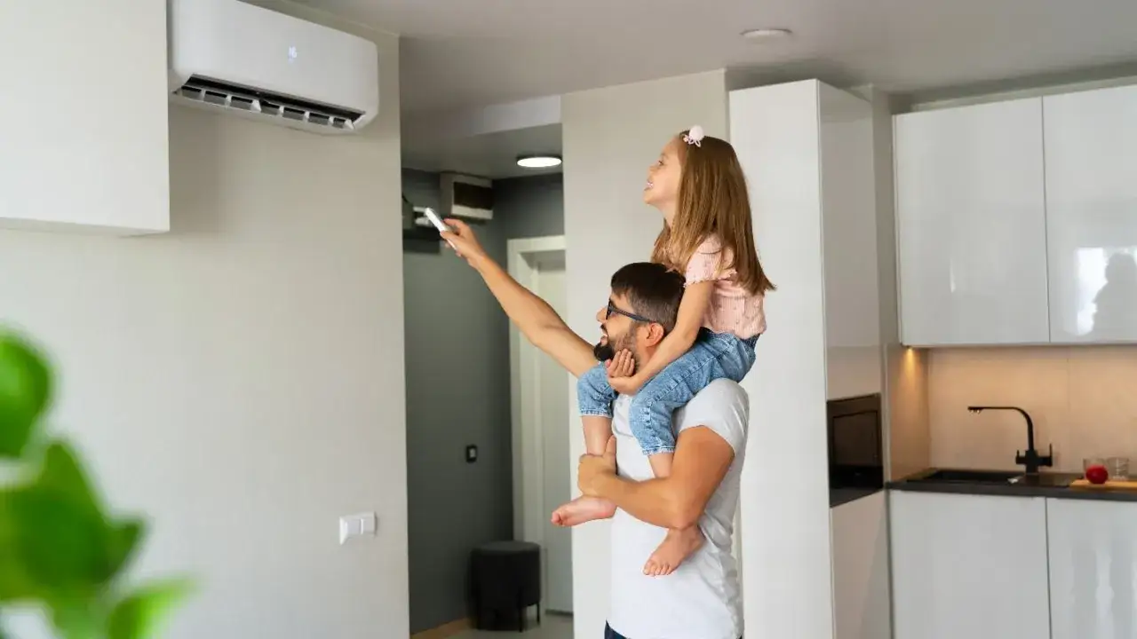 Padre con hija en hombros ajusta el aire acondicionado fijo, decidiendo si es mejor aire acondicionado portátil o fijo para su hogar.