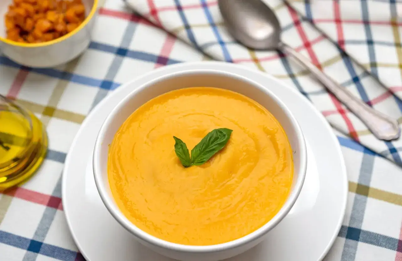 Crema de calabaza, perfecta para tus recetas con calabaza. Servida en un cuenco blanco con hoja de albahaca.