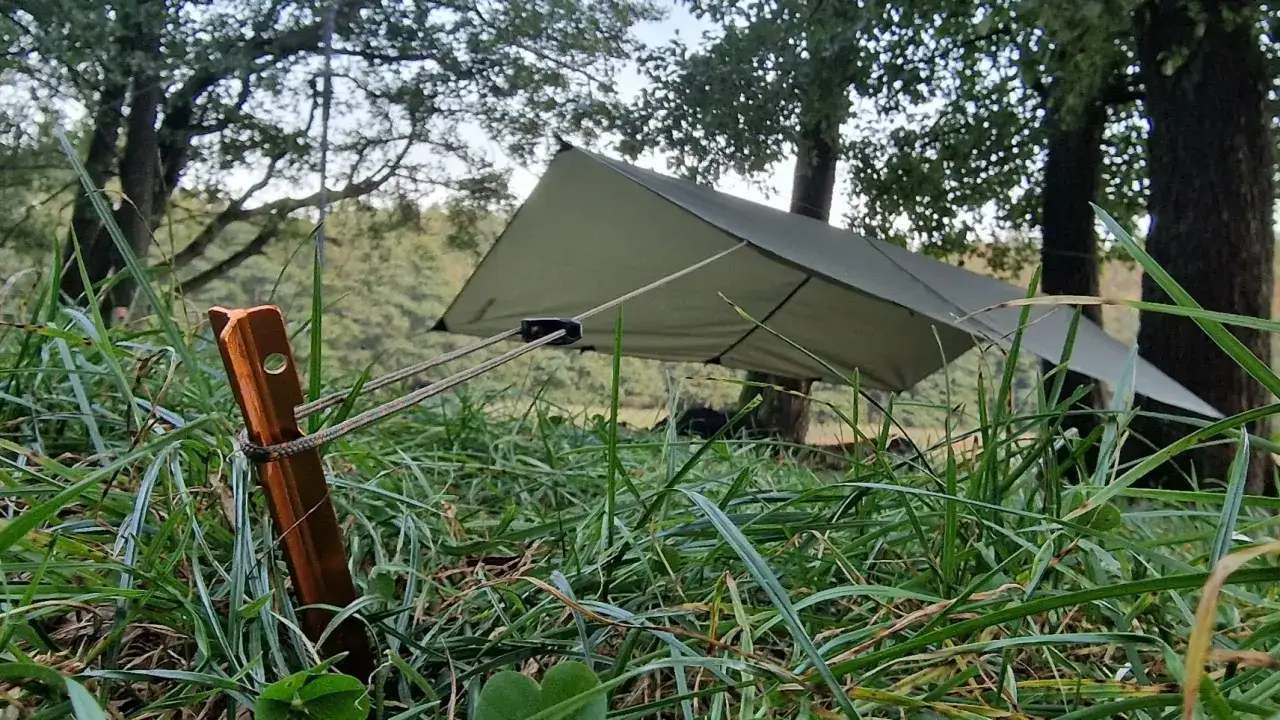 Solidne wiązanie liny do palika namiotowego, naciągające zielony tarp w lesie.
