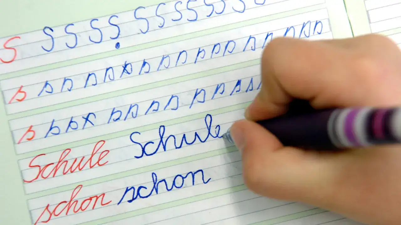Kind &uuml;bt Schreibschrift. Auf dem linierten Blatt sind die **druckschrift buchstaben** S, b und W&ouml;rter wie 