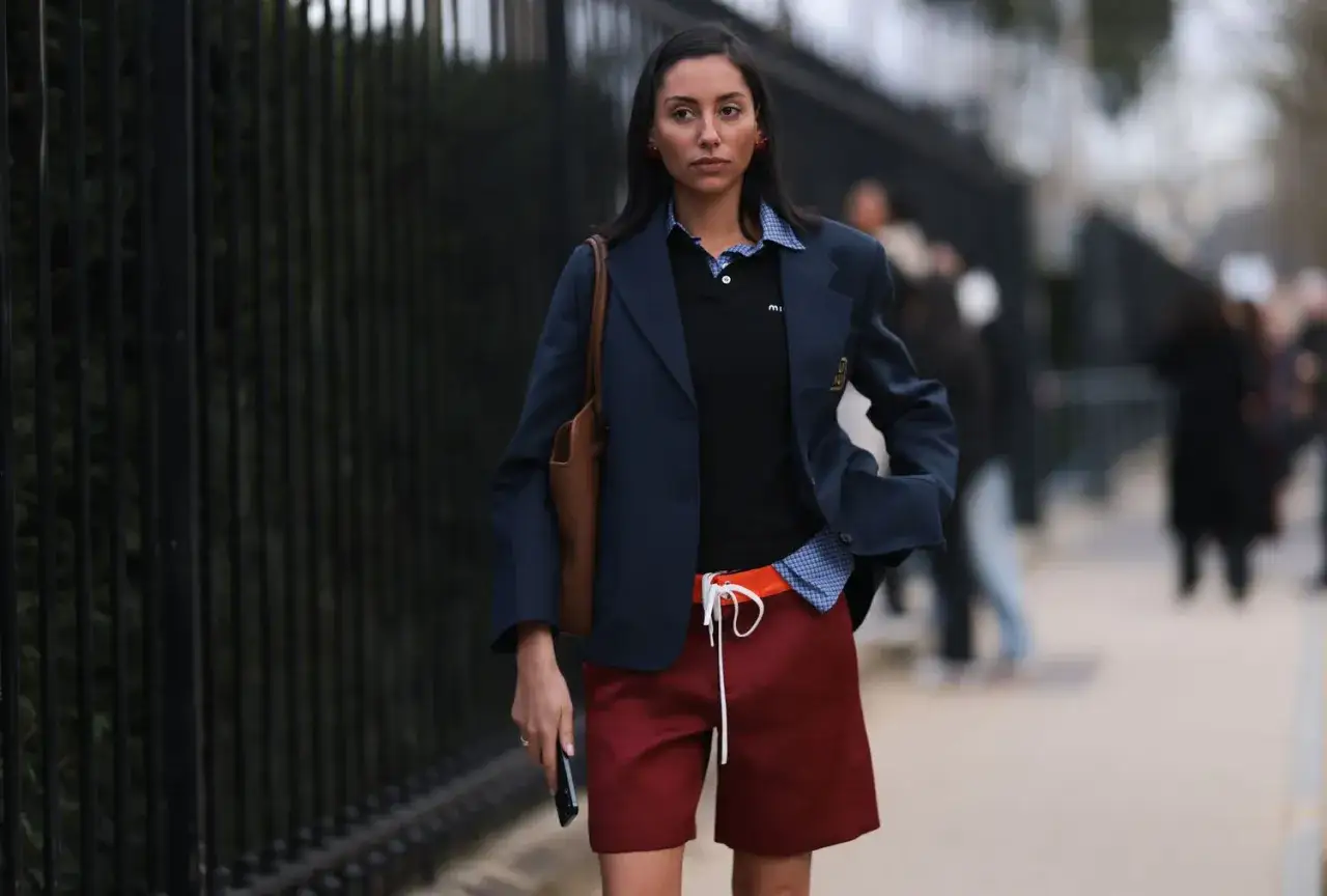 Donna con blazer blu scuro, polo nera, camicia a quadri e shorts bordeaux. Un look audace per capire con cosa abbinare il blu scuro.