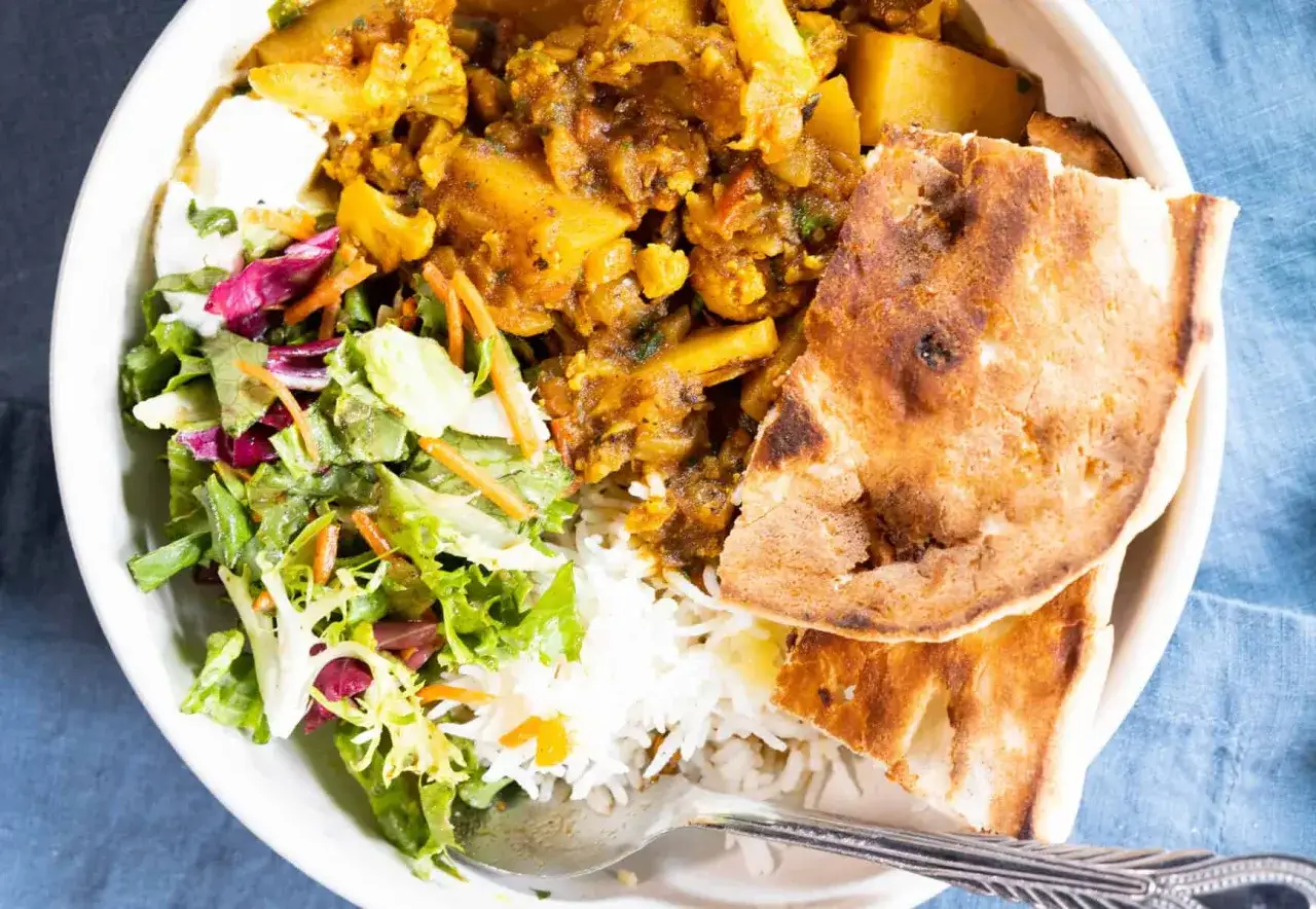 Herzhaftes Aloo Gobi mit Kartoffeln und Blumenkohl, serviert mit Reis, Salat und Fladenbrot.