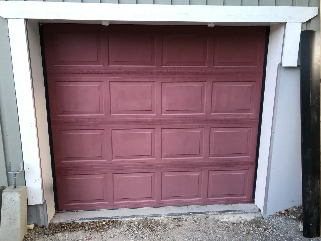 En mörkröd garageport med paneler, redo att måla om för ett fräschare utseende.