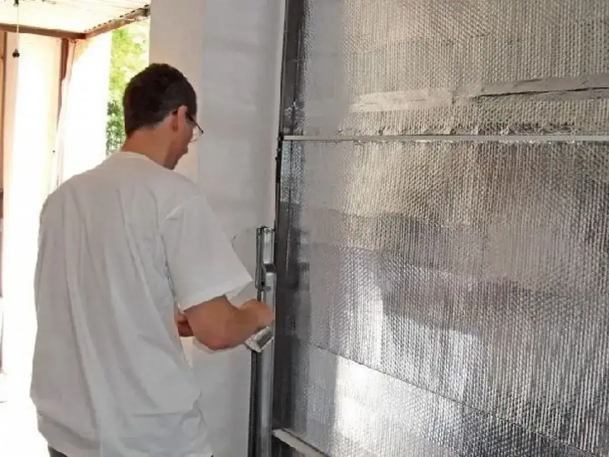 Mężczyzna montuje materiał izolacyjny, poprawiając ocieplenie drzwi garażowych.