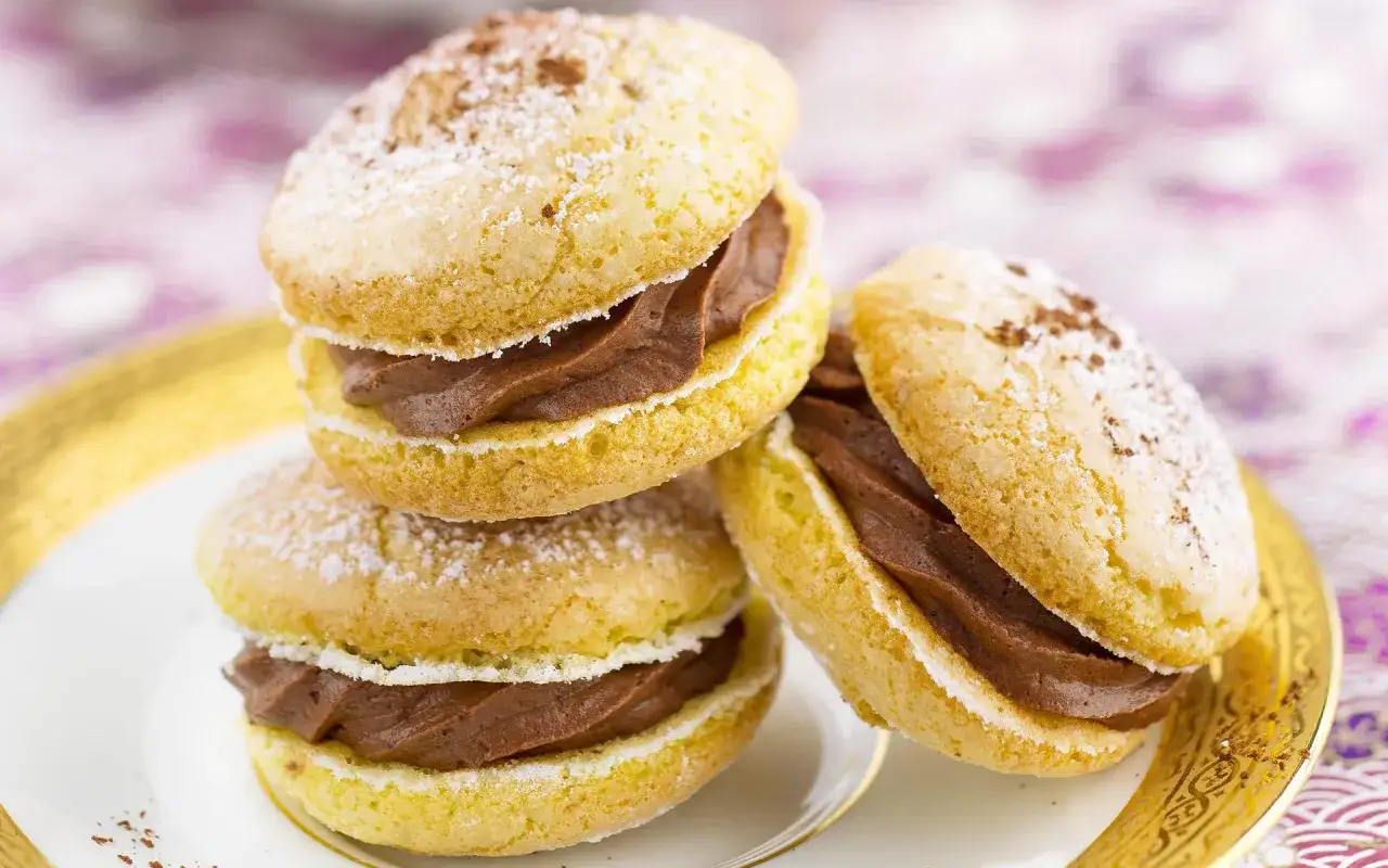 Trois biscuits cuill&egrave;re garnis d'une cr&egrave;me au chocolat, saupoudr&eacute;s de sucre glace et de cacao, sur une assiette dor&eacute;e.
