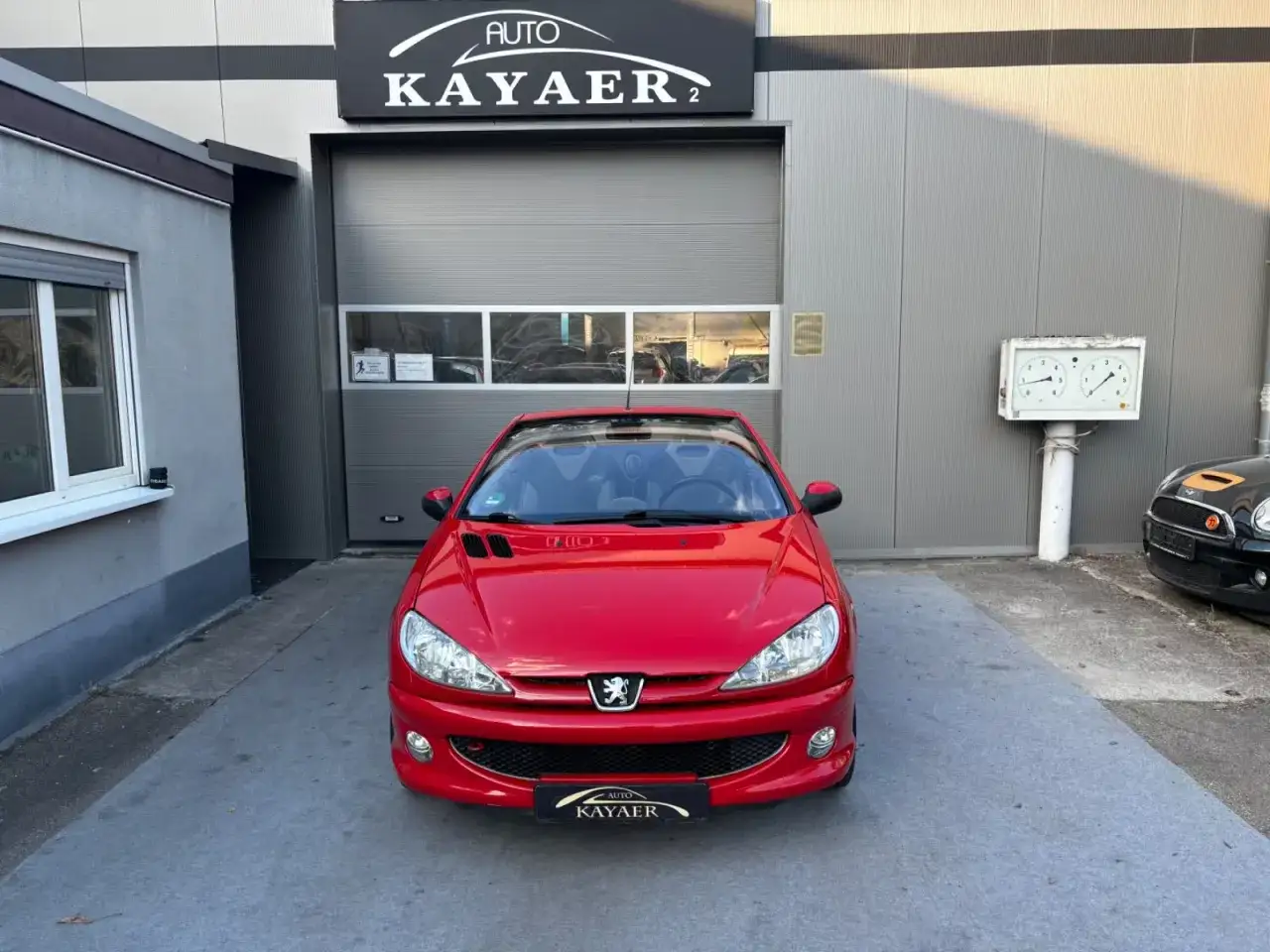 Czerwony Peugeot 206 CC stoi przed salonem samochodowym.