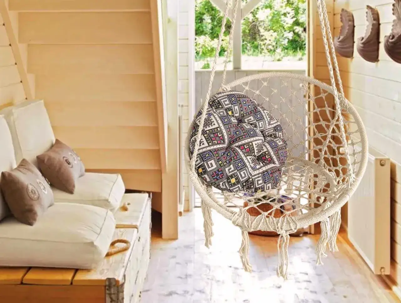 Un columpio de macramé con cojín colorido, ideal para una zona de relax acogedora junto a un sofá de madera.