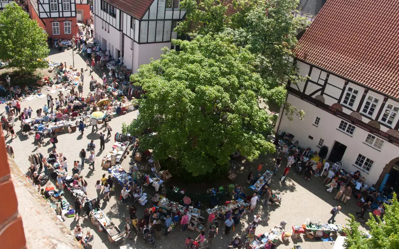 Buntes Treiben auf dem **Flohmarkt Minden**. Menschen schlendern zwischen Ständen mit Kleidung, Büchern und allerlei Trödel.