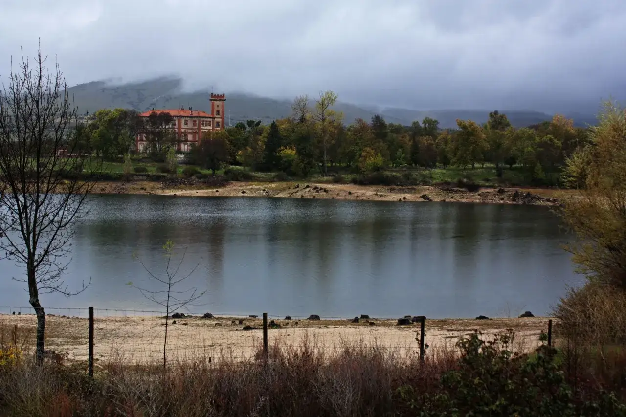Edificio hist&oacute;rico junto al embalse del Pont&oacute;n, rodeado de &aacute;rboles oto&ntilde;ales y colinas nubladas.