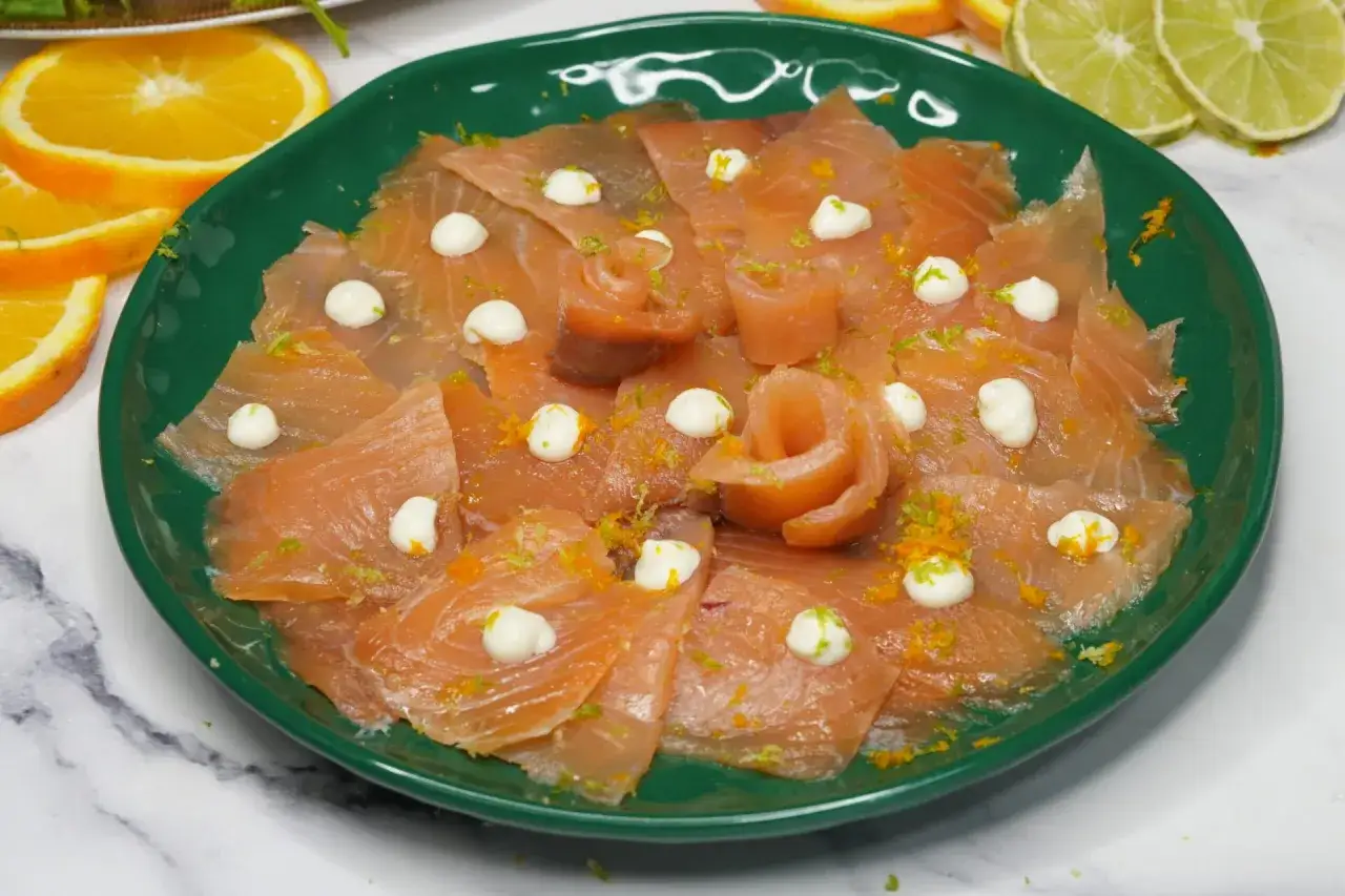 Delicioso salmón marinado casero en un plato verde, decorado con ralladura de cítricos y pequeñas porciones de mayonesa.