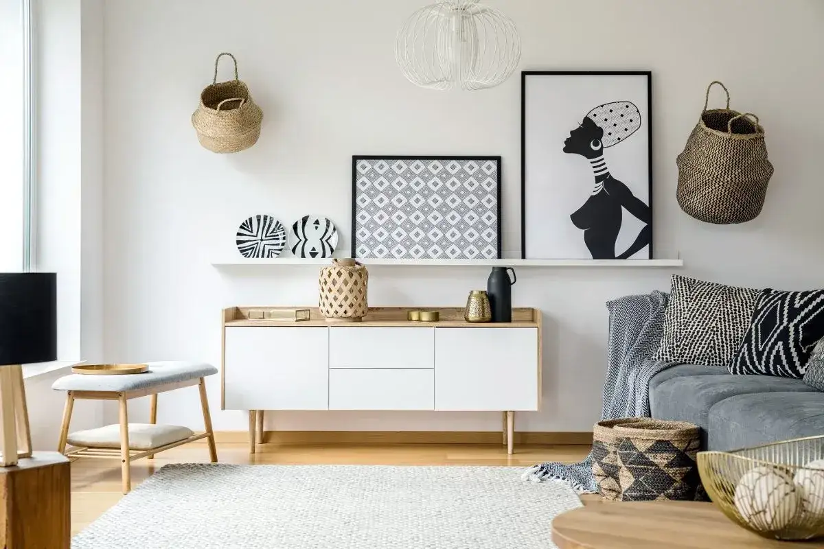 Nowoczesny salon z akcentami etno. Dominują odcienie bieli, czerni i naturalnych materiałów. Na ścianie grafika kobiety i plecione kosze.