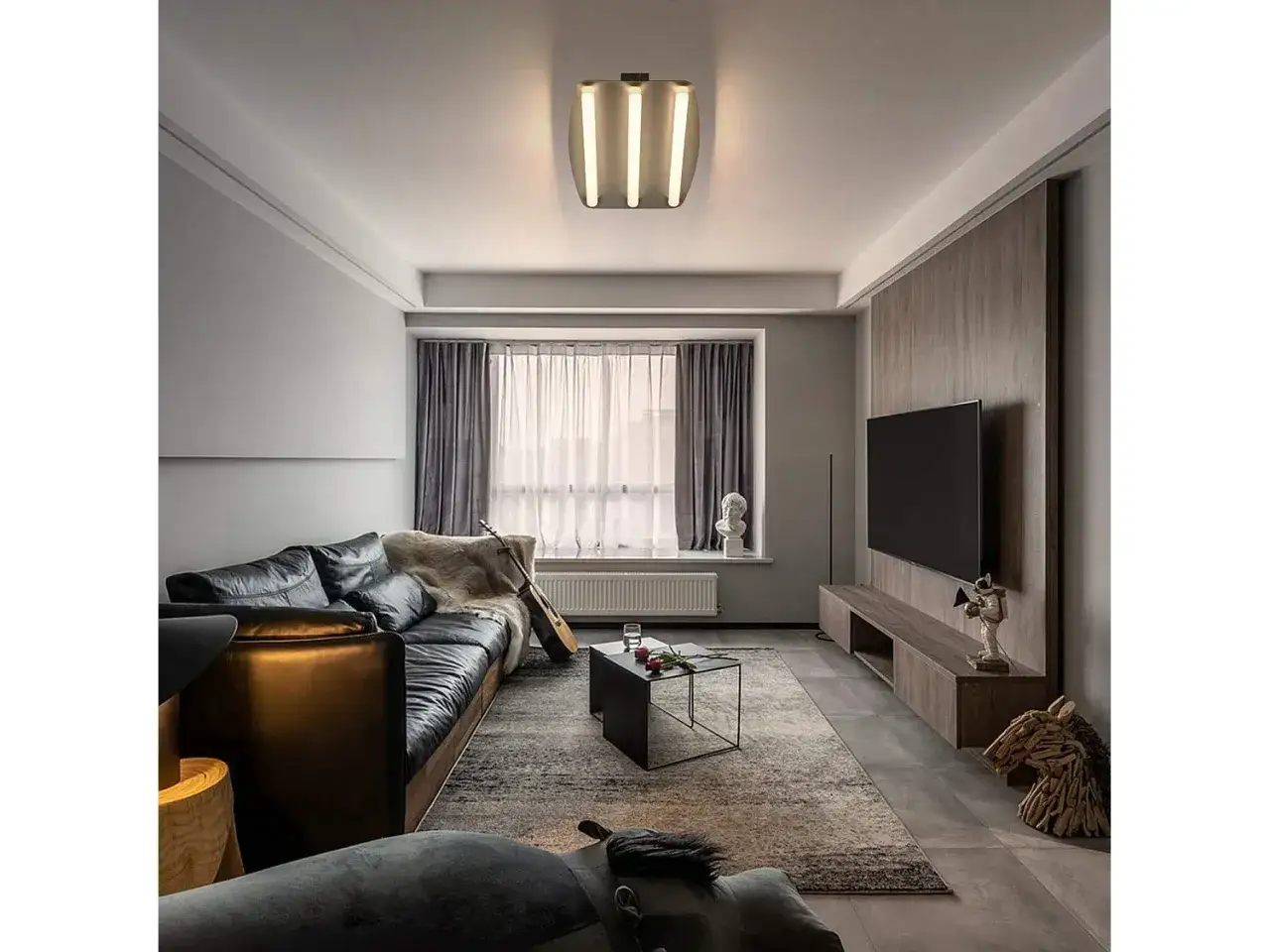 Nowoczesny salon z czarną skórzaną kanapą, dywanem i telewizorem. Nad wszystkim wisi elegancka lampa kwadrat.