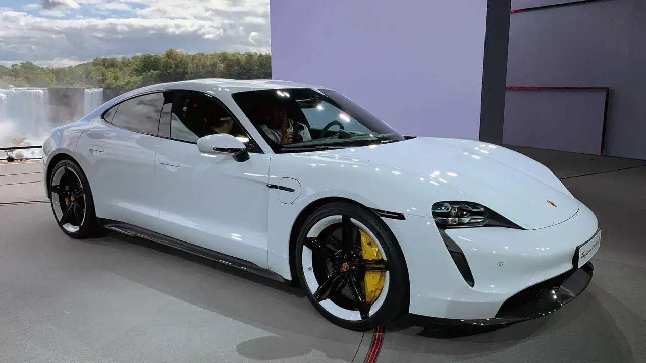 Biały Porsche Taycan z żółtymi zaciskami hamulcowymi na tle wodospadu.