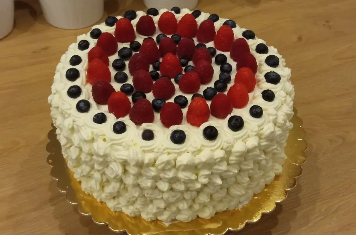 Pyszny tort bezglutenowy ozdobiony bitą śmietaną, malinami i bor&oacute;wkami. Idealny na każdą okazję, a przepis jest prosty!
