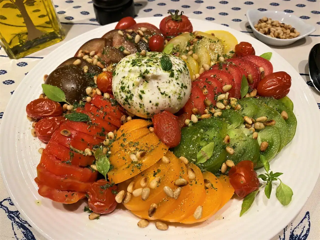 Une magnifique salade de tomates multicolores avec une burrata crémeuse, des pignons de pin grillés et des herbes fraîches. Un délice estival.