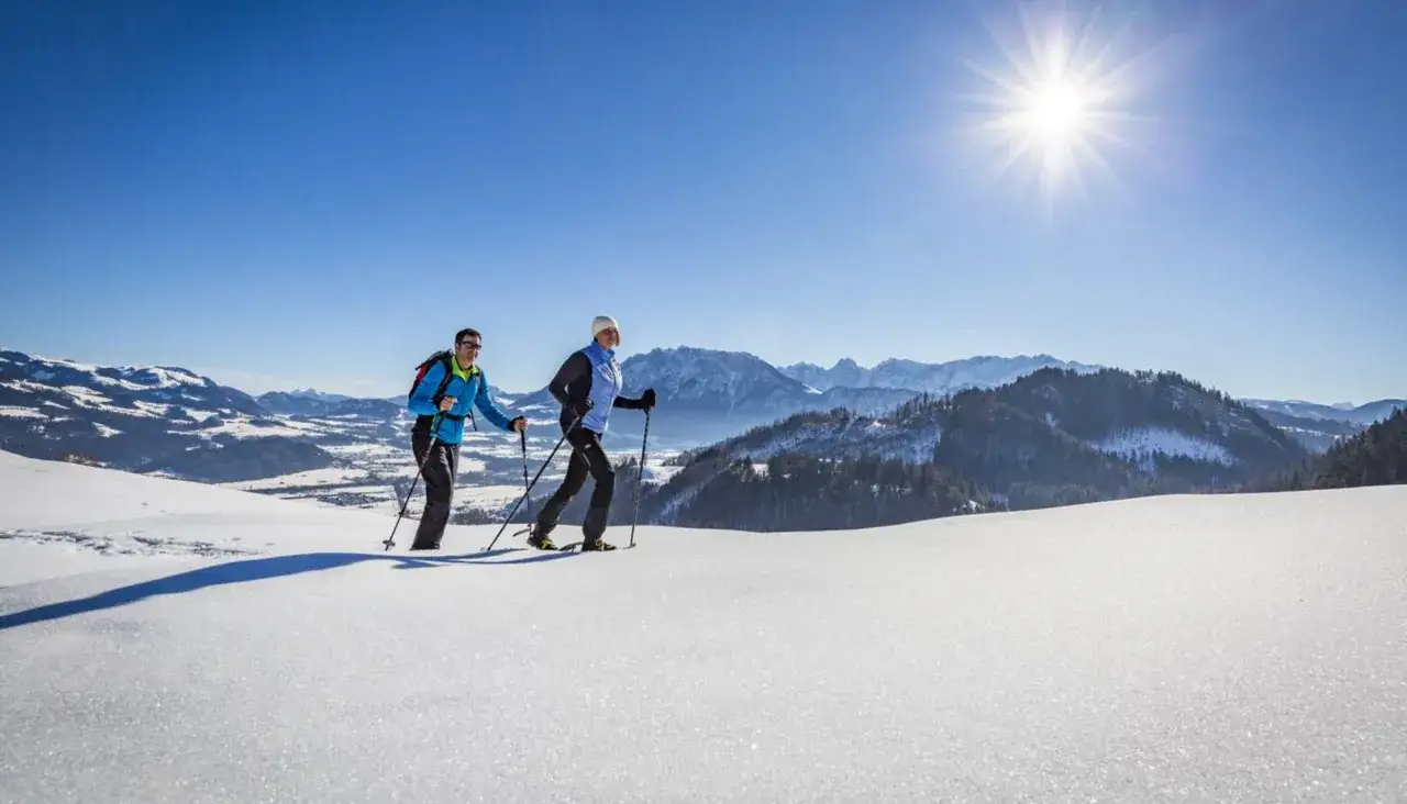 Zwei Wanderer genie&szlig;en die Sonne und die verschneite Landschaft in Bayern im Winter.