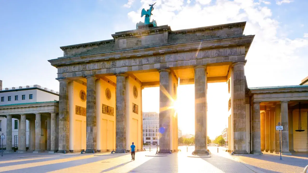 Brandenburger Tor im goldenen Licht, ein beliebter drehorte berlin. Ein Mann geht durch das Tor, die Sonne scheint durch die S&auml;ulen.