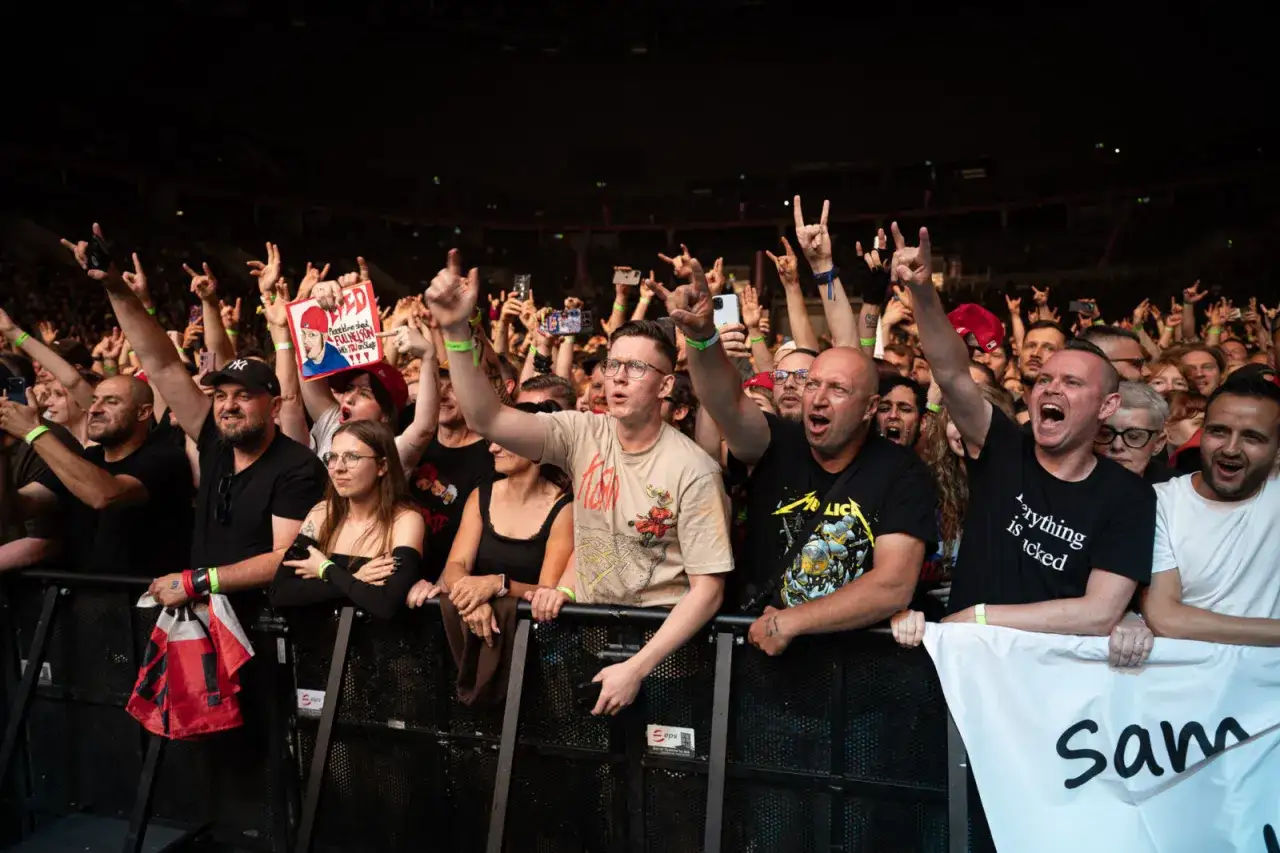Tłum szaleje na koncercie Limp Bizkit, wznosząc ręce i śpiewając.