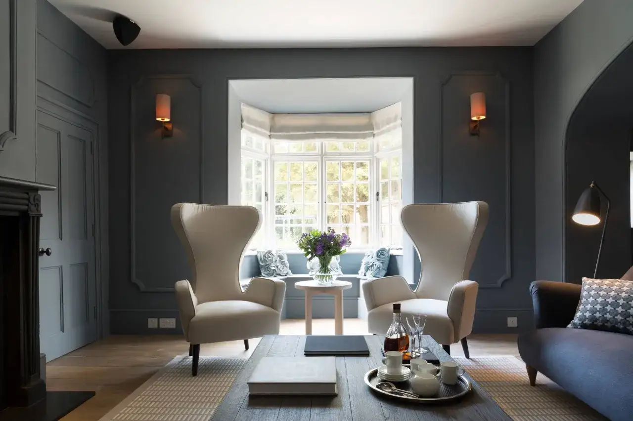 Dos sillones orejeros blancos junto a un ventanal. Ideas para como tapizar un sillon orejero y renovar tu sala.