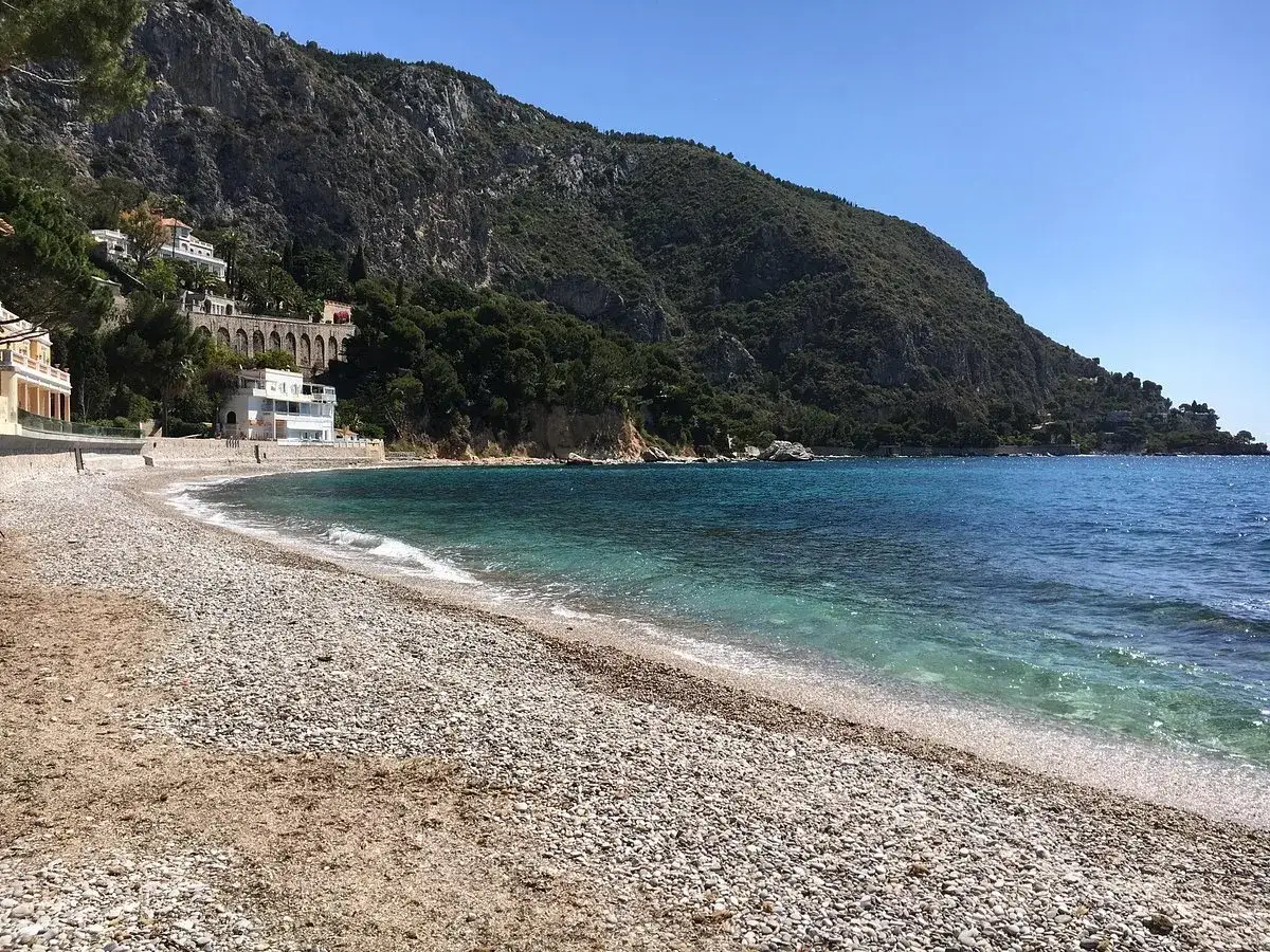 Spiaggia di ciottoli a Eze sur Mer, con acque turchesi e ville aggrappate alla scogliera verdeggiante.
