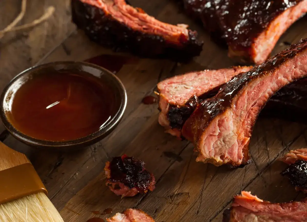 Soczyste żeberka BBQ na drewnianej desce, obok miseczka z sosem i pędzelek. Idealne do marynowania żeberka.