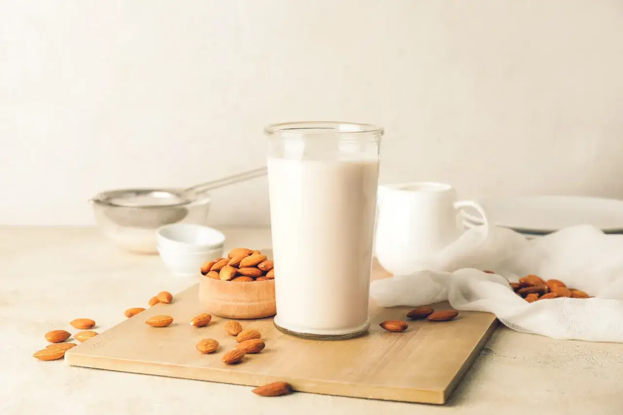 Un bicchiere di latte di mandorla fatto in casa, con mandorle in una ciotola e sparse sul tagliere.
