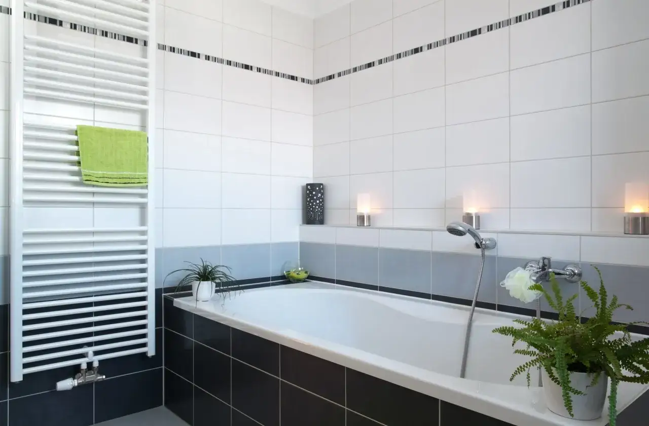 Salle de bain moderne avec baignoire, radiateur blanc et pose de fa&iuml;ence soign&eacute;e. Une serviette verte ajoute une touche de couleur.