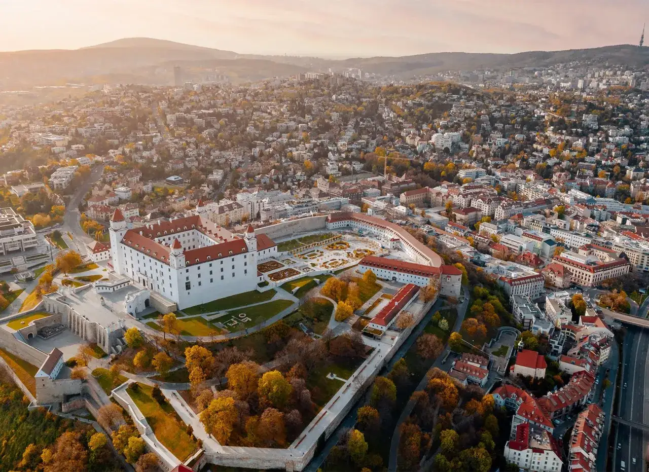 Bratysławski zamek g&oacute;ruje nad jednym z największych miast Słowacji, otoczony jesiennymi drzewami i rozległą panoramą miejską.