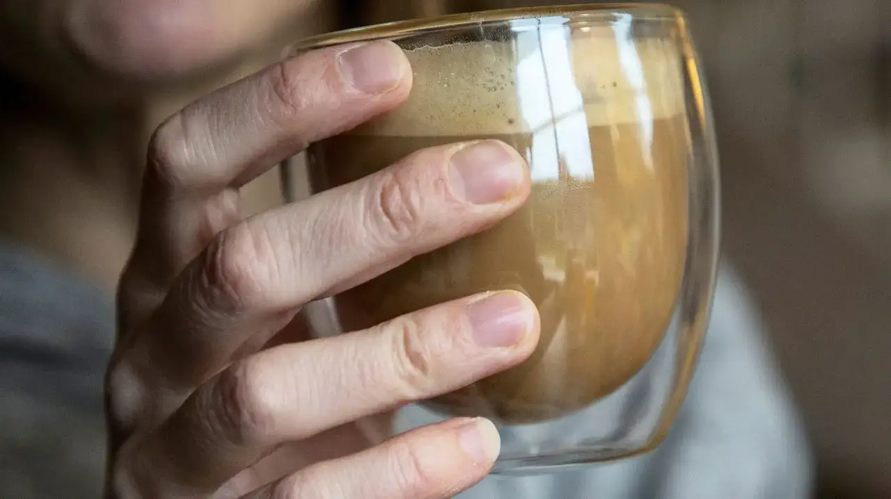 En hand h&aring;ller ett glas med kaffe. Kanske dags att sluta med kaffe depression och hitta nya rutiner.