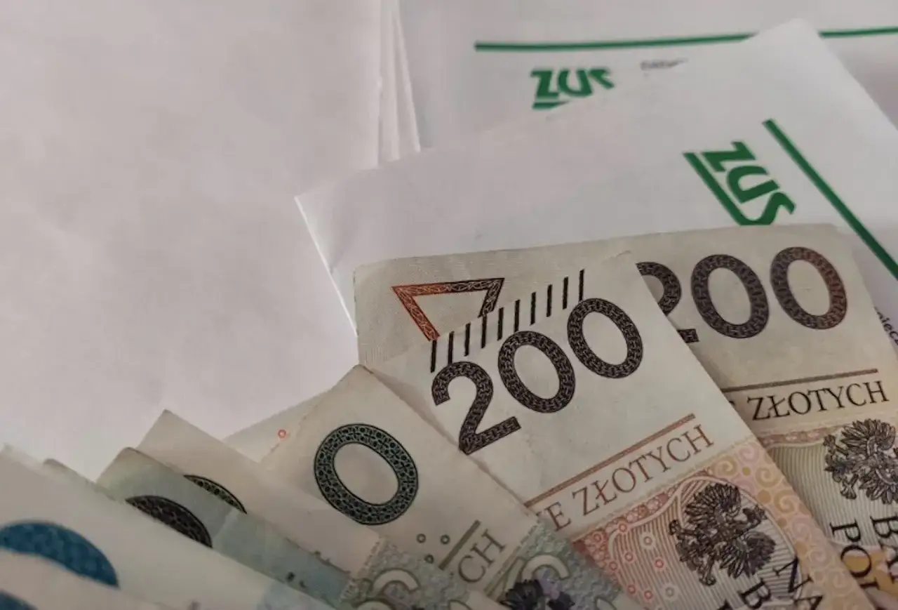 Pieniądze, banknoty 200 zł, leżą na dokumentach ZUS. Może to być zwrot podatku lub świadczenie 300 plus.