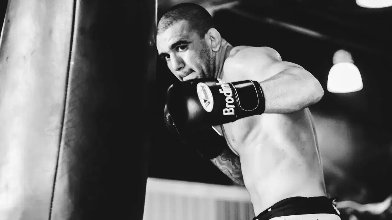 A boxer throws a powerful body hook, sweat glistening on his skin as he trains intensely in the ring.