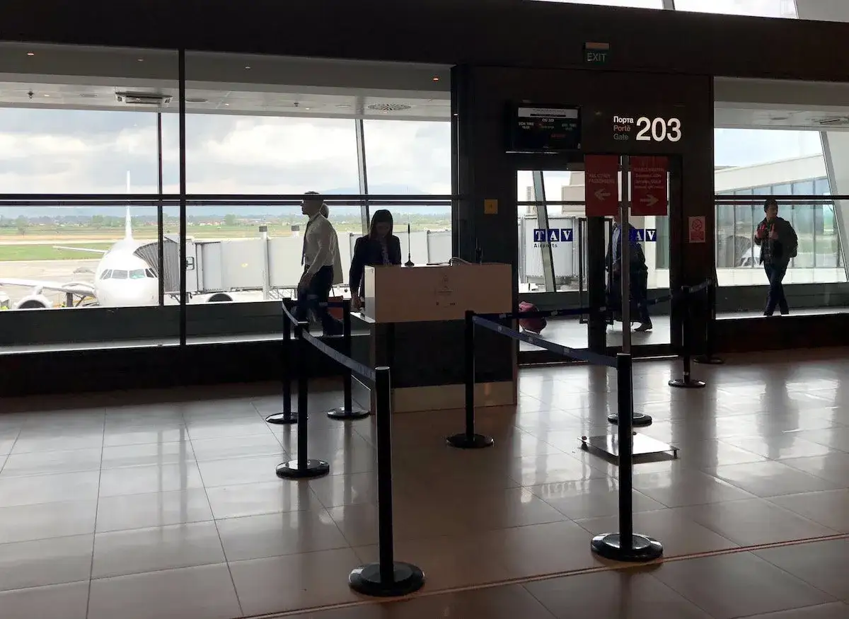 Brama 203 lotniska, z samolotem przy rękawie. Kolejka do odprawy, z możliwością **priority boarding**.