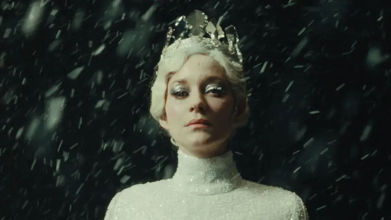 Marion Cotillard w białej, błyszczącej sukni i koronie, w deszczu śniegu. Scena jak z jej filmów.