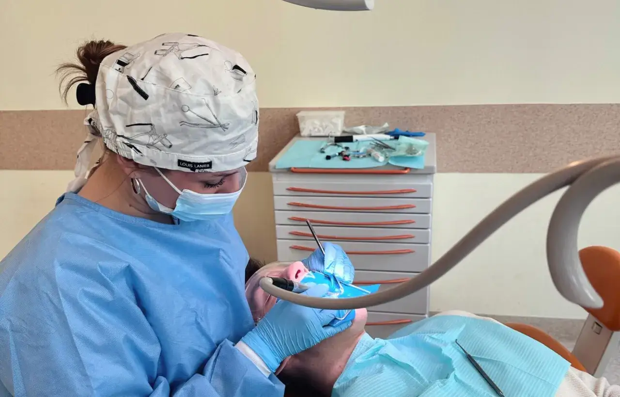 Studentka stomatologii w czepku z motywem narzędzi dentystycznych pracuje przy pacjencie.