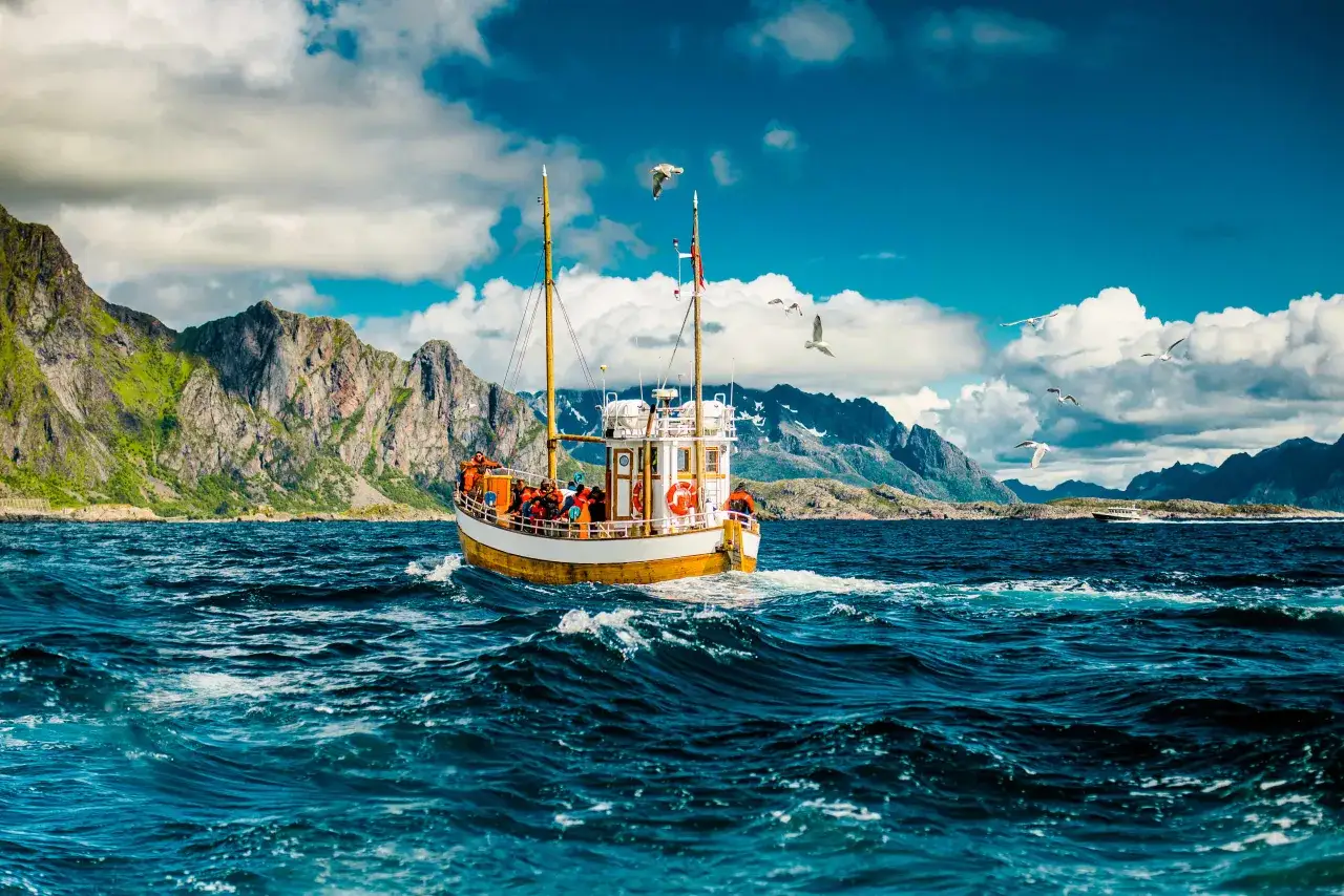 Båt med passagerare på havet i Norge, med dramatiska berg i bakgrunden. En perfekt dag för havsfiske i Norge.