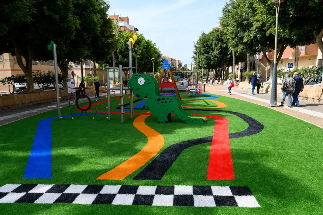Divertida zona verde en Almer&iacute;a con un tobog&aacute;n de dinosaurio y caminos de colores sobre c&eacute;sped artificial.