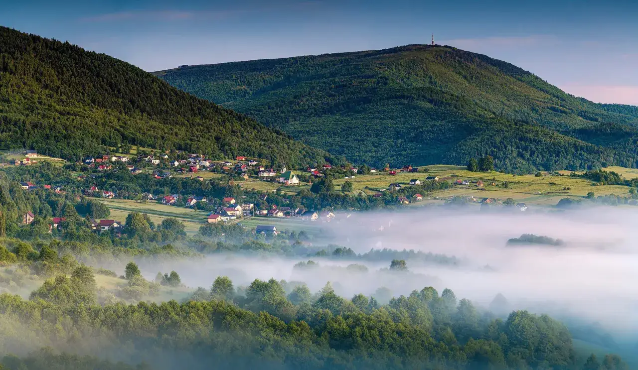Poranna mgła otula dolinę z domkami, a w tle wznoszą się zielone wzgórza. Bielsko Biała jakie góry? To Beskid Mały.