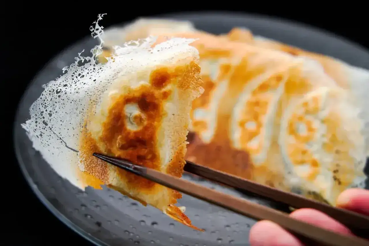 Chrupiące japońskie pierożki gyoza, złociste i apetyczne, podniesione pałeczkami.