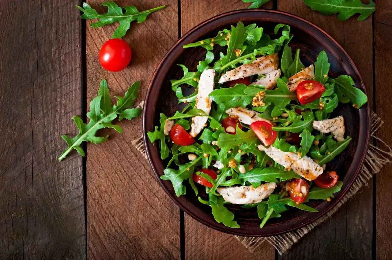 Deliziosa tagliata di pollo su letto di rucola, pomodorini e semi di senape, su un tavolo di legno rustico.