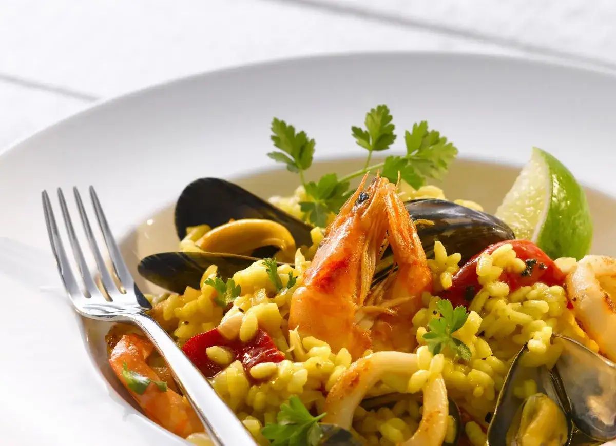 Pyszne risotto z owocami morza: krewetki, małże, kalmary i ryż, udekorowane natką pietruszki i ćwiartką limonki.