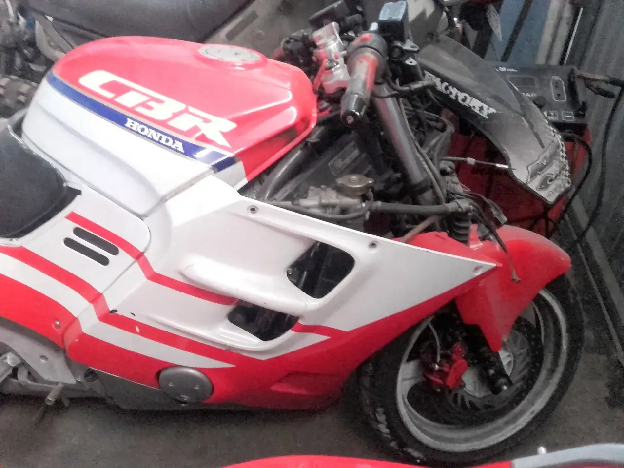 Czerwono-biały motocykl Honda CBR 1000F w warsztacie, z widocznym silnikiem i przednim kołem.