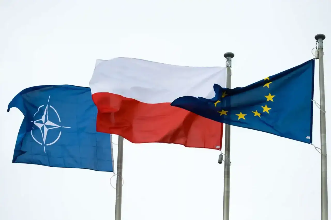 Flaga Polski, flaga NATO i flaga Unii Europejskiej powiewają na maszcie.