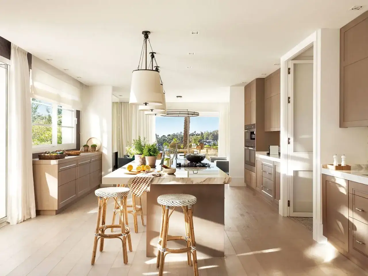 Cocina luminosa con isla central, taburetes de mimbre y vistas al exterior. Ideas para como dise&ntilde;ar una cocina moderna y funcional.