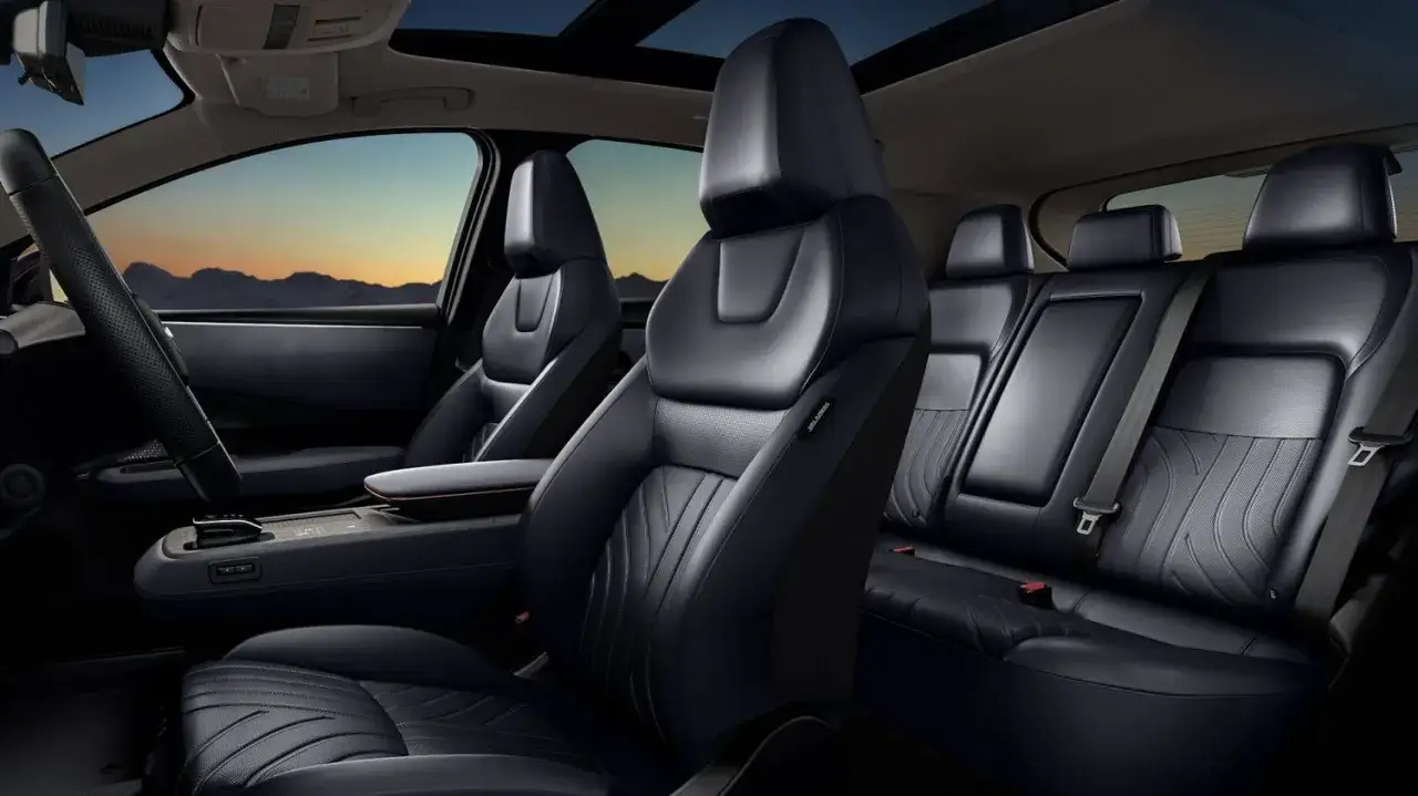 Interior del Nissan Ariya con asientos de cuero negro, volante y consola central. El atardecer se ve a través del techo panorámico.