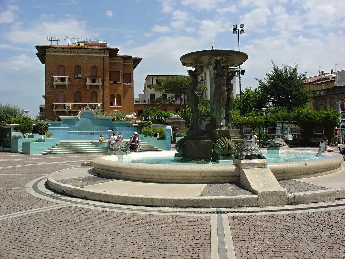 Fontana con statue e tartarughe a Cattolica, Emilia Romagna. Persone sedute vicino a una fontana azzurra.