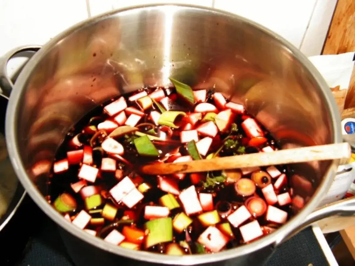 Sauerbraten einlegen in Rotwein mit Gemüse. Ein Holzlöffel liegt in der Marinade.