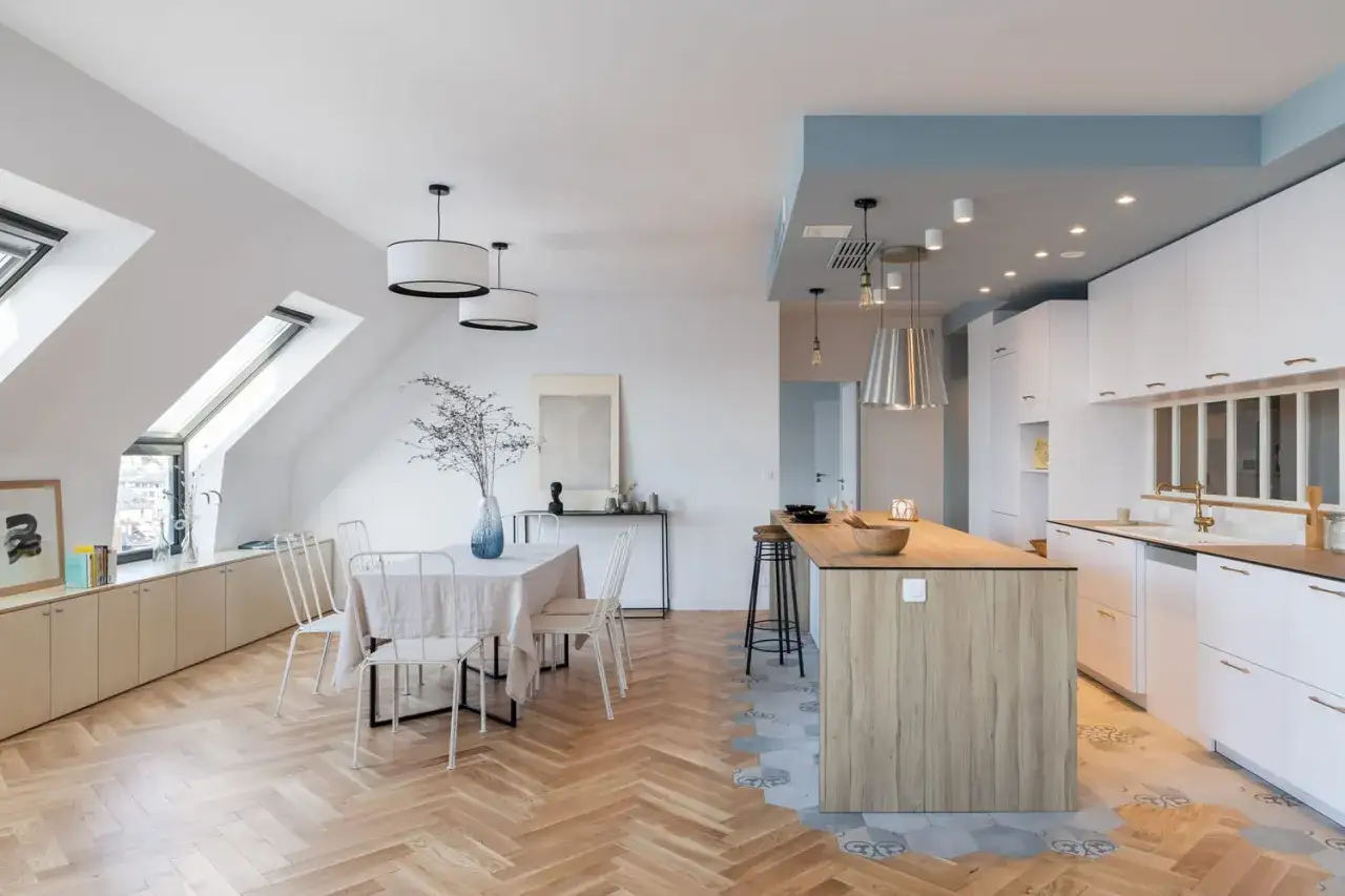 Un salon-cuisine moderne avec un sol en parquet à chevrons et un sol carrelé hexagonal devant le plan de travail.