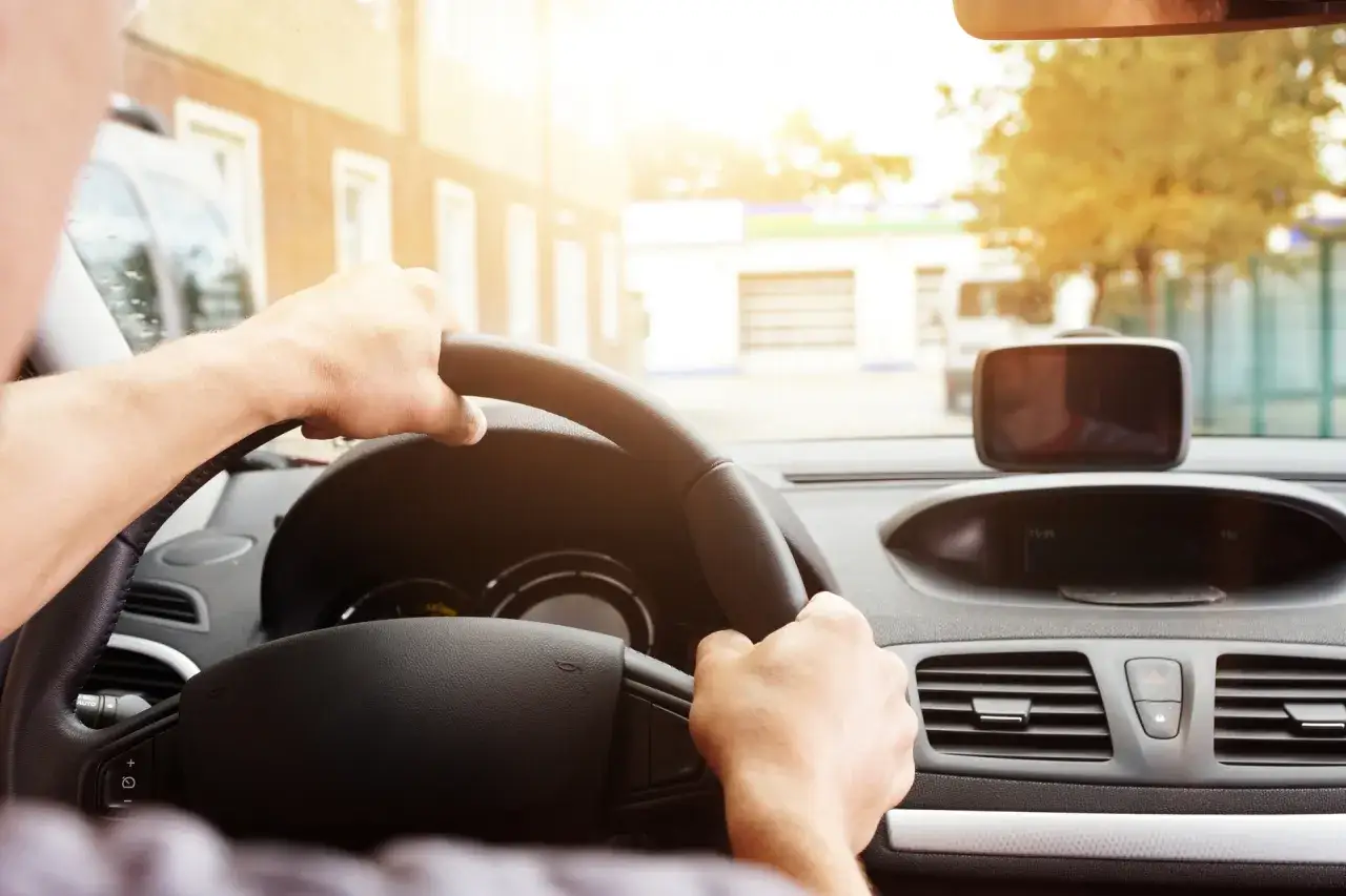 Dłonie na kierownicy, czuć lekkie drgania przy 120 km/h. Słońce świeci przez przednią szybę.